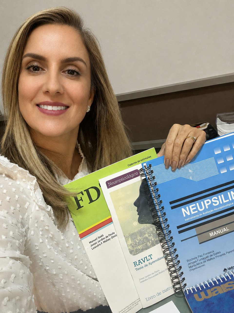 Taciana Albuquerque segurando manuais e cadernos de instrumentos de avaliação neuropsicológica